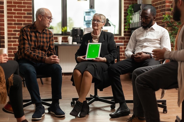 Psichiatra in una riunione che mostra tablet con schermo verde a un gruppo di persone. specialista della donna alla sessione di terapia utilizzando chroma key con sfondo isolato e modello di mockup sul display.