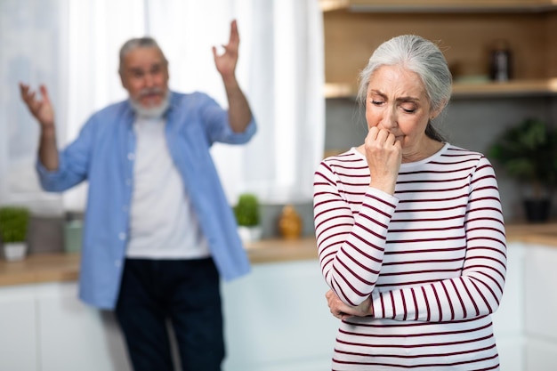 Psychological Abuse Upset Senior Woman Crying In Kitchen While Arguing With Husband