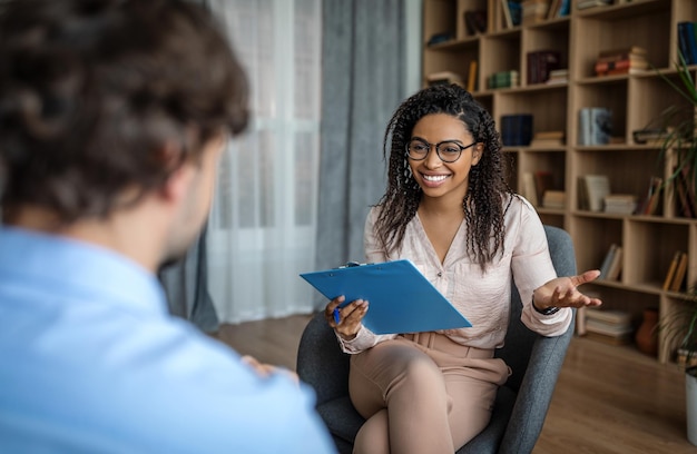 Photo psychological therapy cheerful pretty young african american female psychologist in glasses talking with european man