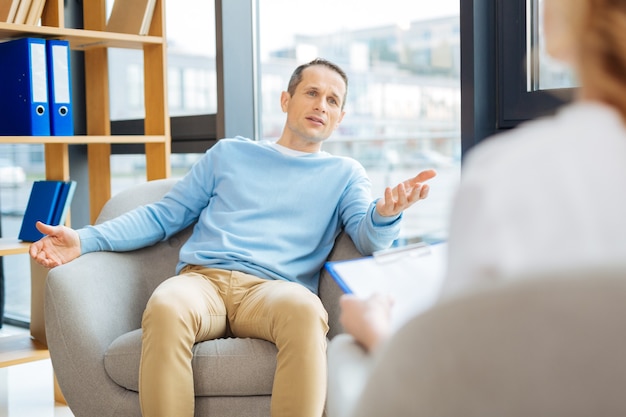 Psychologische therapie. Leuke aangename knappe man zittend in de fauteuil en praten met zijn arts tijdens psychologische therapie