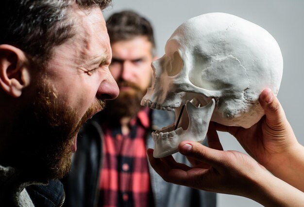 Psychology concept. Human fears and courage. Looking deep into eyes of your fear. Man brutal bearded hipster looking at skull symbol of death. Overcome your fears. Be brave. Focused on breaking fear.