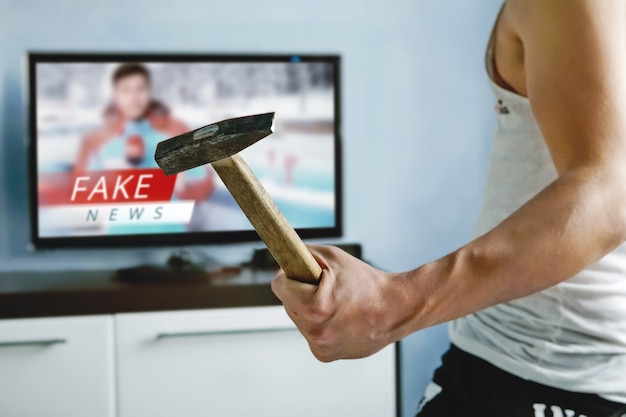 Photo a psychopath wants to crash the tv with a hammer. the viewers got tired of false news. truth misrepresented in the news on a modern tv. fake news report. zombie tv. deception of viewers.