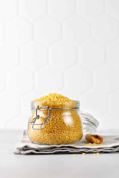 Ptitim Uncooked ptitim pasta in a jar with wooden spoon on napkin Israeli couscous Tile copy space