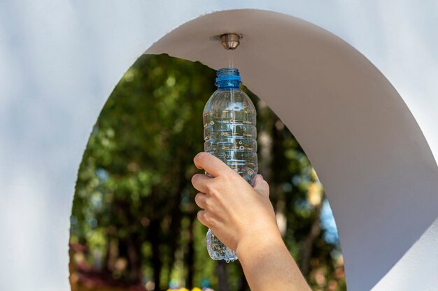 Public free drinking water fountain . Female pouring water to bottle