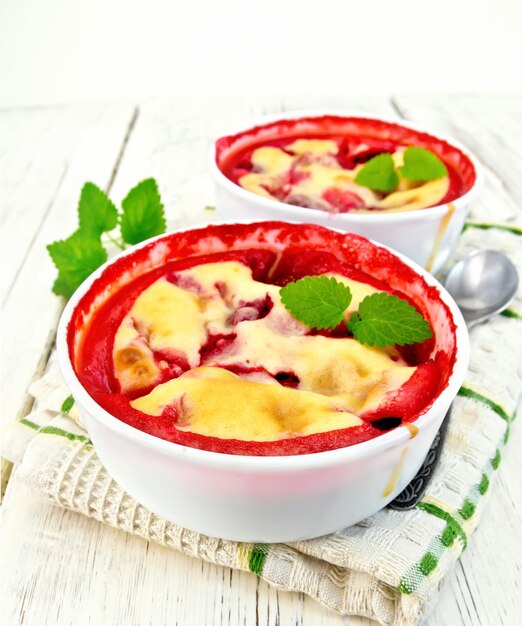 Pudding strawberry in two bowls with berries and mint on a napkin on a light wooden planks