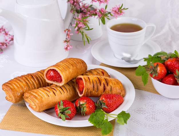 puff pastries stuffed with strawberries, on a white dish, with a cup of tea, on a light background