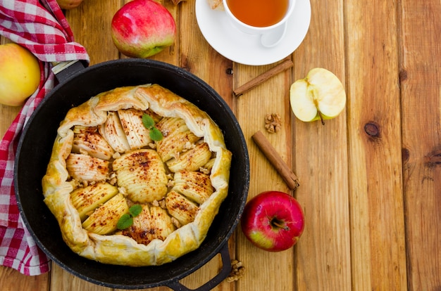 Crostata di mele con cannella, noci e caramello in padella su un tavolo di legno scuro