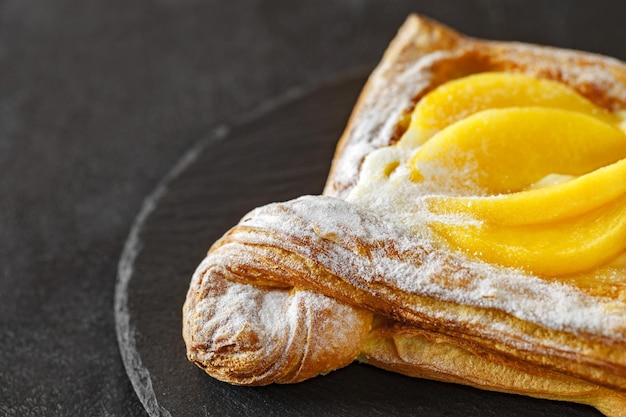 Puff pastry cake with peaches cream and powdered sugar on slate stone plate round selective focus side viewxD