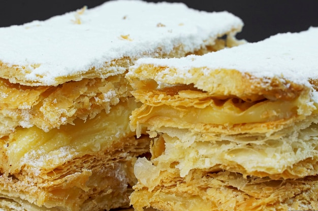 Puff pastry cakes with powdered sugar and cream on wooden board. Selective focus.