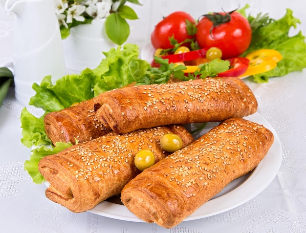 puff pastry pies with sesame seeds lettuce and tomatoes on a light background