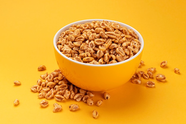 Puffed wheat cereal in bowl on yellow background, honey air rice