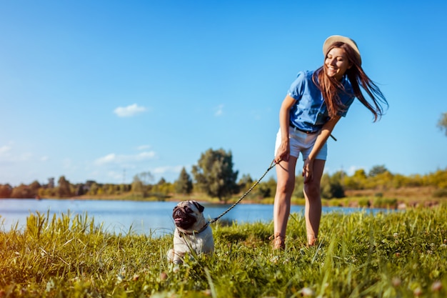 川のそばに座ってパグ犬。マスターの命令を待っている幸せな子犬。犬と女が屋外で低温