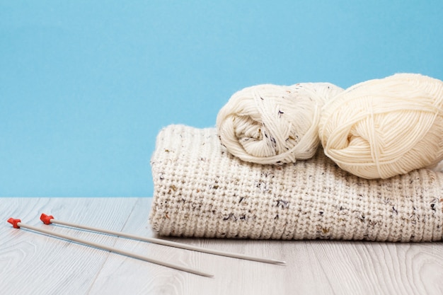 灰色のボードと青い背景に金属編み針で毛糸のプルオーバーとかせ。編み物のコンセプト。