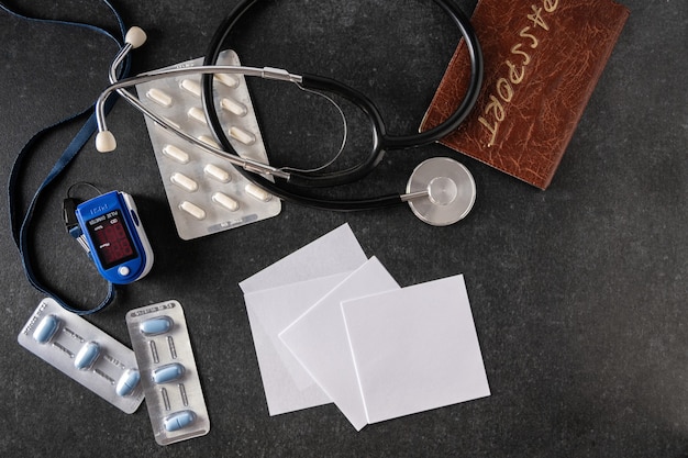 Pulse oximeter, blood oxygen meter, electronic thermometer, passport, tonometer, pills on a gray surface