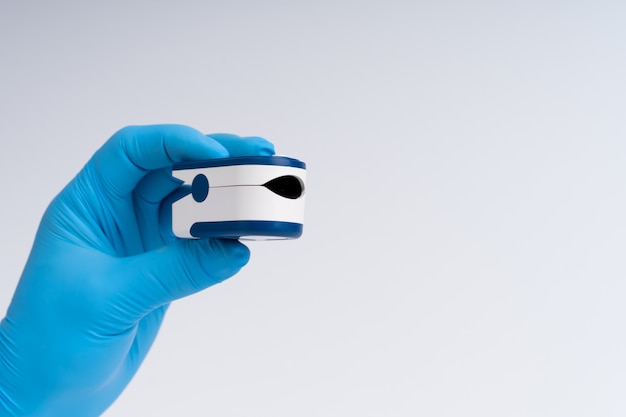 Pulse oximeter on a white background. A hand in a medical glove holds a device for health diagnostics.