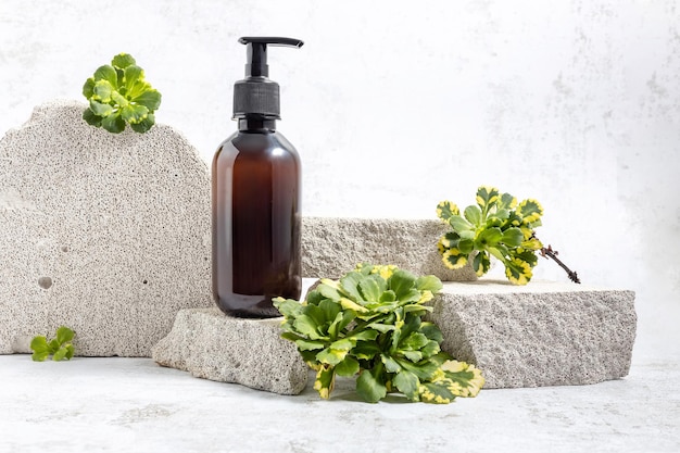 Pump bottle on a podium made of stones and green succulent leaves on a gray background