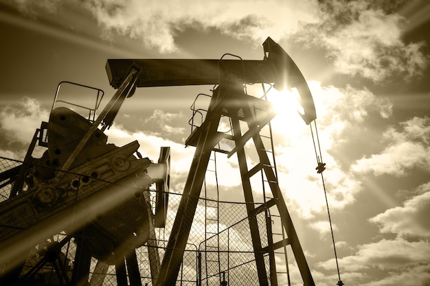 Pump jack on a sky and sun background. Extraction of oil. Toned sepia.