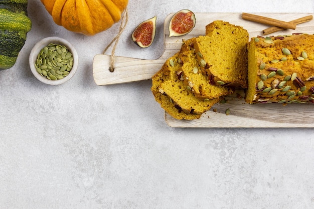 Pumpkin bread, cake on a wooden cutting board with pecan nuts, pumpkin seeds and cinnamon spices on a light gray background with colorful pumpkins and figs. Top view. Copy space.