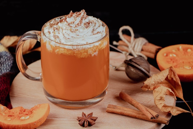 Pumpkin coffee latte with whipped cream on dark background Hot autumn drink with cinnamon and spices in glass mug on a wooden tray