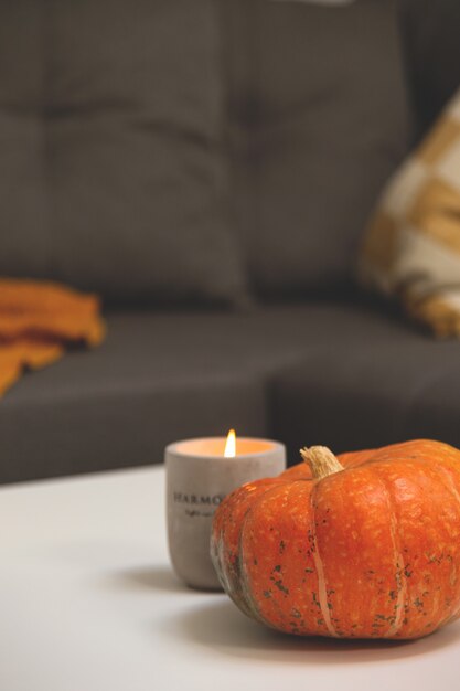 Pumpkin and concrete candlestick on table in living room next to sofa with pillows and blanket autum...