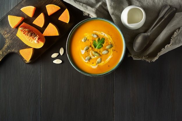 Pumpkin cream soup in a bowl with pumpkin seeds, parsley, cream and pumpkin slices on wooden table