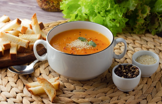 Crema di zucca in una tazza bianca con crostini di pane, sesamo e spezie