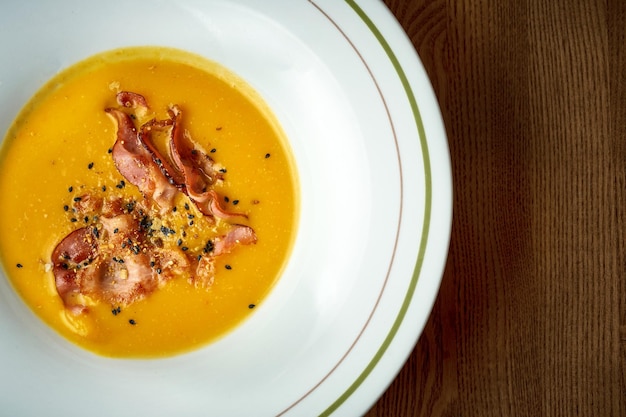 Pumpkin cream soup with bacon in a plate on a wooden background