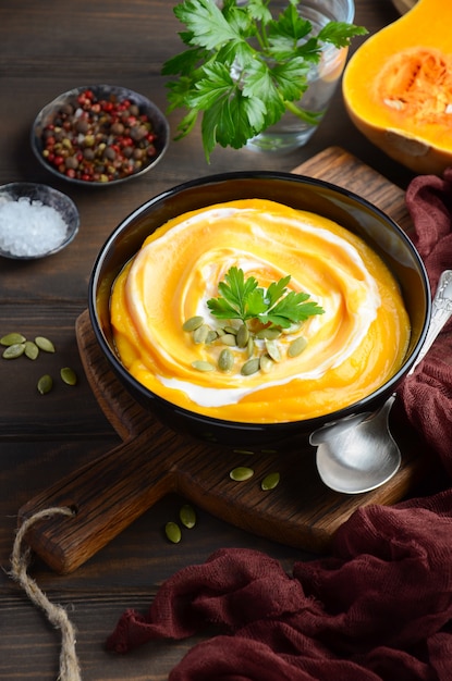 Pumpkin cream soup with cream and pumpkin seeds on wooden table.