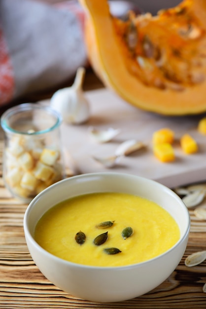 Pumpkin cream soup with seeds in a bowl on a wooden table.