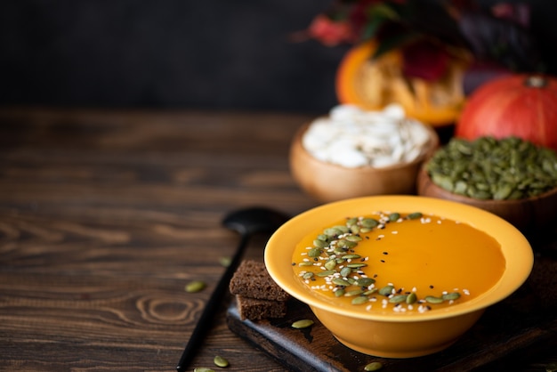 Тыквенный крем-суп с семенами и кунжутом в желтой тарелке на деревянном столе