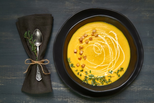 Pumpkin creme soup in black ceramic bowl on dark, flat lay