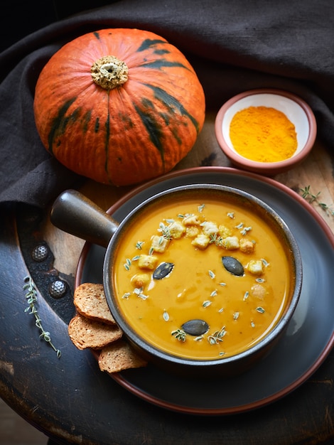 Pumpkin creme soup in ceramic bowl seasoned with pumpkin seads, thyme and croutons on dark