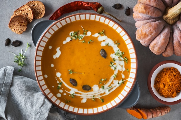 Pumpkin creme soup in ceramic bowl seasoned with thyme, cream and croutons, ingredients all around