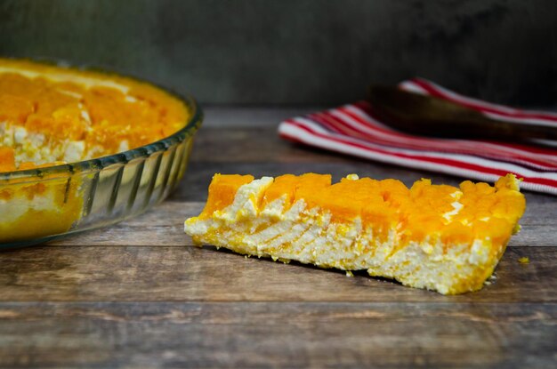 Pumpkin curd casserole. Slice of pumpkin cheesecake next to platter of pie on wooden background