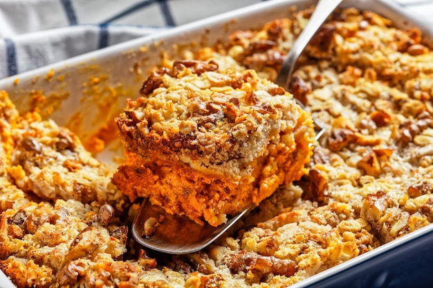 Pumpkin dump cake with traditional pumpkin pie spices: cinnamon, clove, nutmeg with walnuts and rolled oats on top served on a baking dish on white marble background, top view, close-up