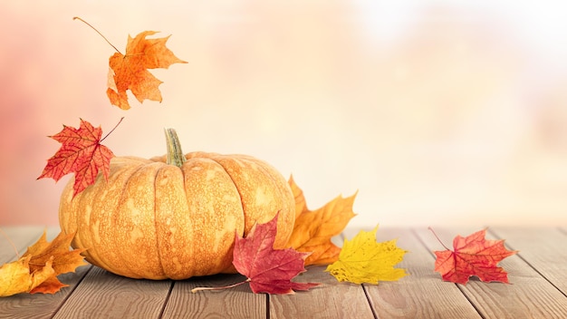 Pumpkin and falling autumn leaves on a wooden table