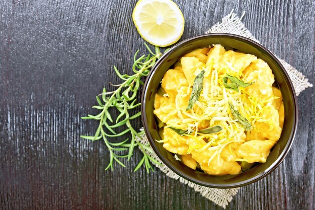 Pumpkin gnocchi with sage, lemon, cheese and butter in a bowl on burlap against dark wooden board on top