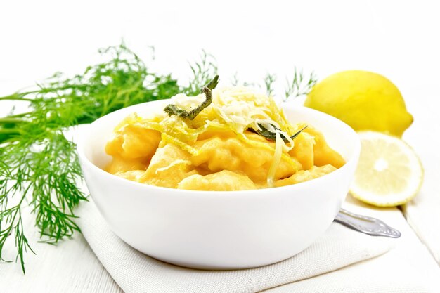 Gnocchi di zucca con salvia, limone, formaggio e burro in una ciotola su un asciugamano sullo sfondo di assi di legno