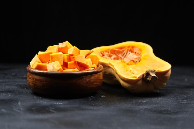 Pumpkin half fresh pieces in wooden bowl on black background Cooking vegetable dish