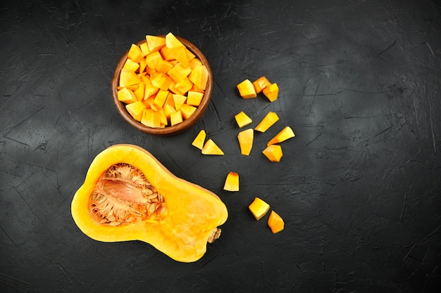 Pumpkin half fresh pieces in wooden bowl on black background