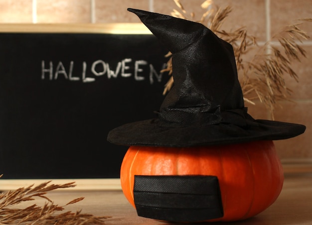 pumpkin in a hat and mask on the background of a black board with the inscription Halloween