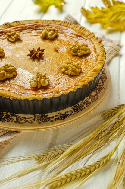 Pumpkin homemade vegan pie and spices cinnamon, anis, orange pumpkins with yelllow dry autumn leaves decor on dark table background.