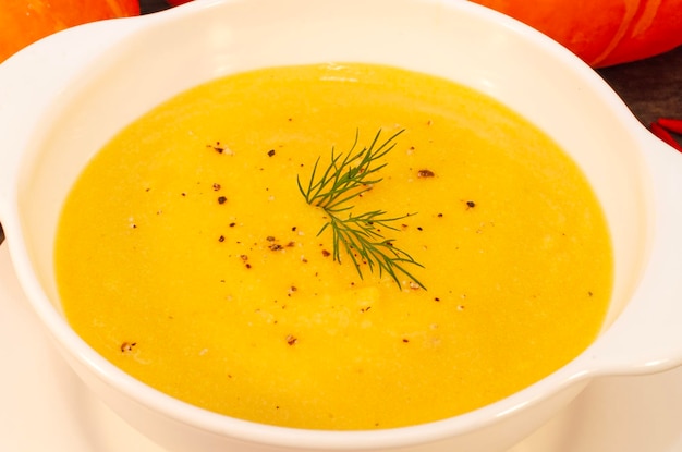 Pumpkin hot soup puree and pumpkins on a wooden table