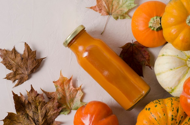 Succo di zucca in una bottiglia di close-up su uno sfondo autunnale con foglie di acero,