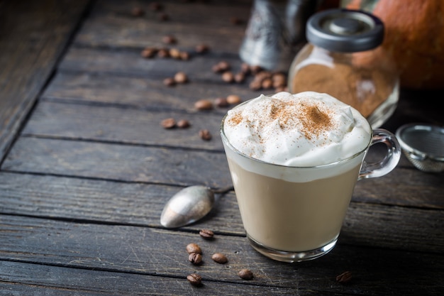 Pumpkin latte with whipped cream and spices, with pumpkins over wood texture.