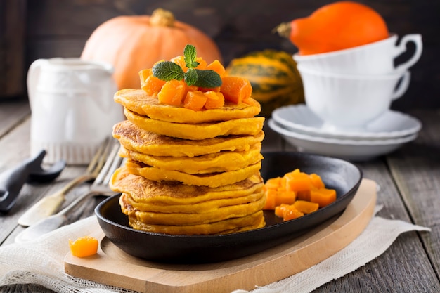 Pumpkin pancakes with mint leaves and sauce on the old wooden surface. Rustic style. Selective focus.