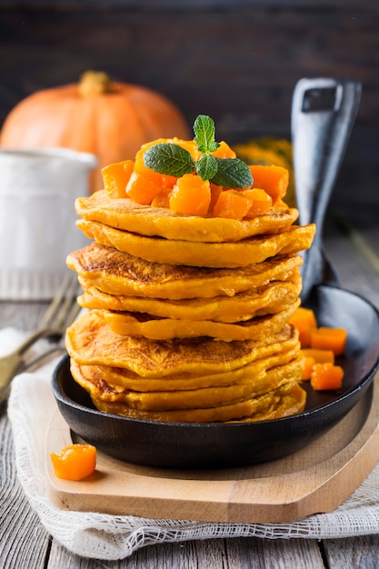 Pumpkin pancakes with mint leaves and sauce on the old wooden surface. Rustic style. Selective focus.