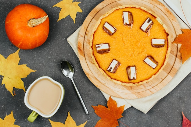 Тыквенный пирог на деревянной доске, маленькие оранжевые тыквы, осенние кленовые листья и чашка кофе