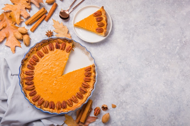 Pumpkin Pie and slice  with pecan nut and cinnamon on gray concrete background, top view, copy space. Homemade autumn pastry for Thanksgiving