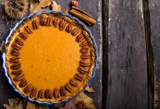 Pumpkin Pie with pecan nut and cinnamon on rustic background, top view, copy space. Homemade autumn pastry for Thanksgiving